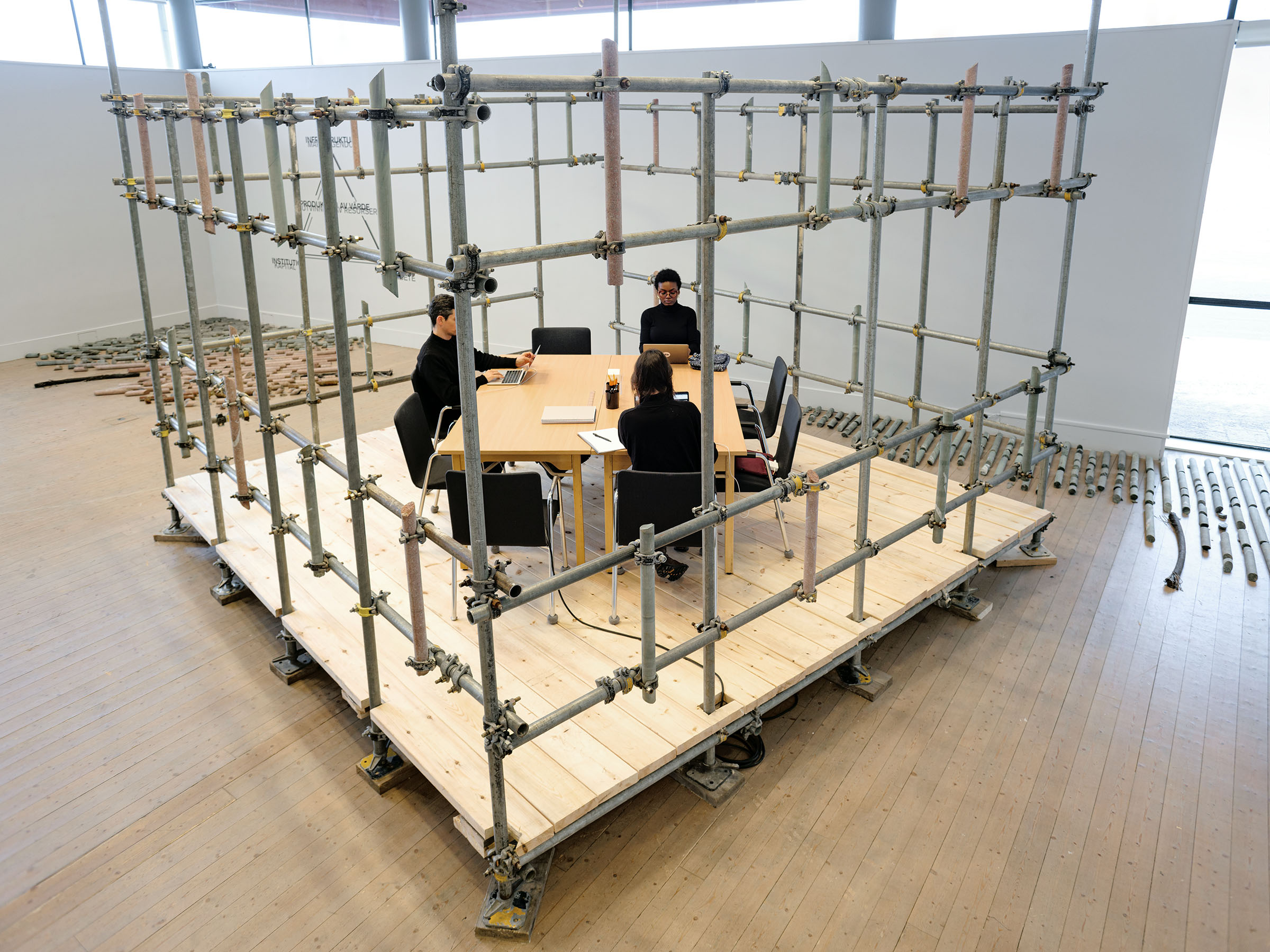 A scaffolding with rock core samples and people working inside. An artwork by Daniel de Paula at Luleå Konsthall, a part of the Luleå Biennial curated by Bruno Alves de Almeida and Aude Christel.